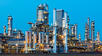 A large petrochemical plant at dusk. Distillation towers and other installations are visible against blue sky.
